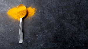 Turmeric spice in spoon over dark stone table background. Top view with copy space